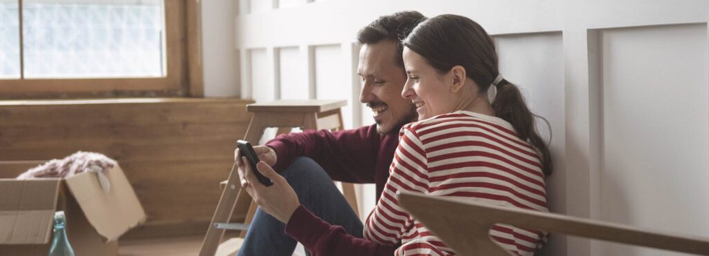 Pareja de jóvenes sentados en suelo mirando el móvil y riéndose